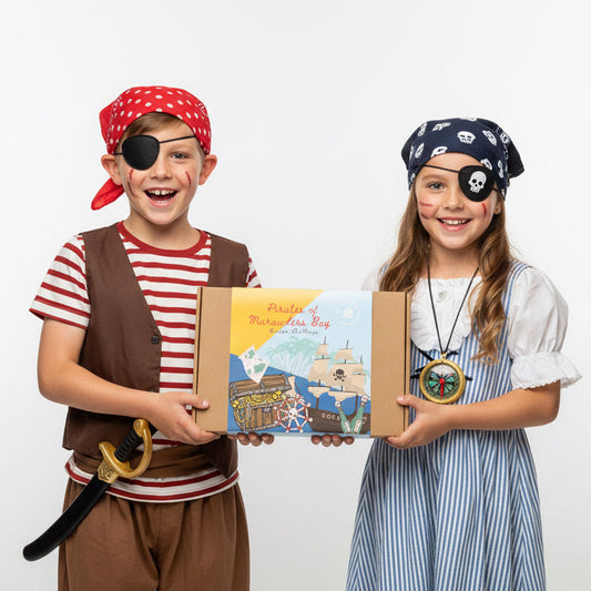 Two children in pirate costumes holding an escape room game box called “pirates of marauders bay”